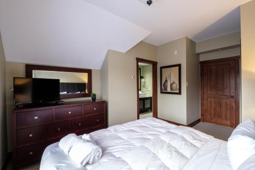 a bedroom with a bed and a dresser with a television at Étoile du Matin by Rendez-Vous Mont-Tremblant in Mont-Tremblant