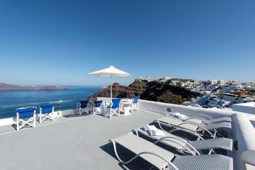 Un balcón con sillas, una sombrilla y el océano. en Vallas Apartments & Villas en Firostefani