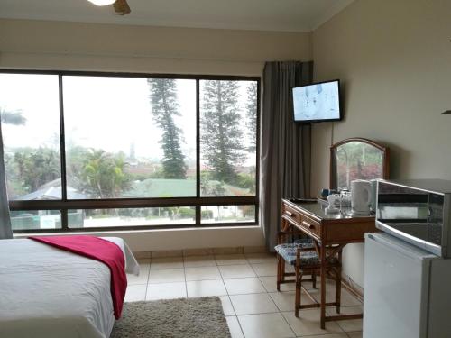 a hotel room with a bed and a desk and a window at Rockview Guest House in Port Edward