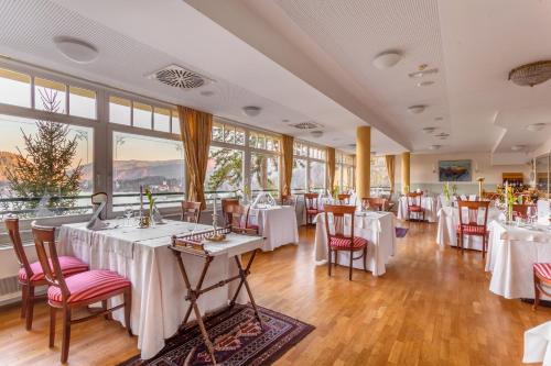 um restaurante com mesas e cadeiras brancas e janelas em Hotel Triglav em Bled