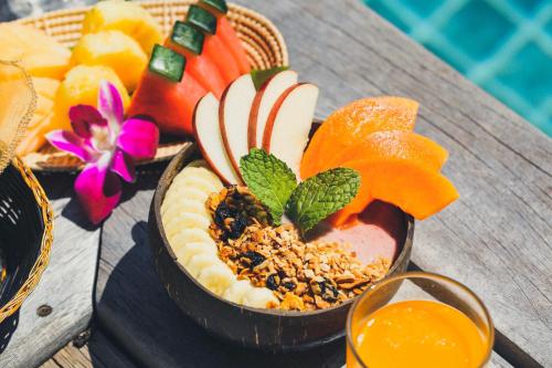 a wooden table with a bowl of fruit and a drink at Tango Luxe Beach Villa, Koh Samui in Choeng Mon Beach