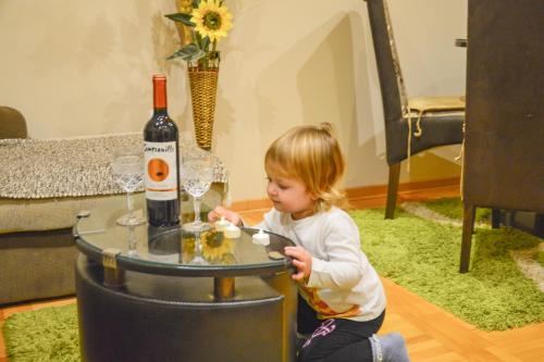 a little girl sitting next to a table with a bottle of wine at Apartments Josipovic in Zlatibor
