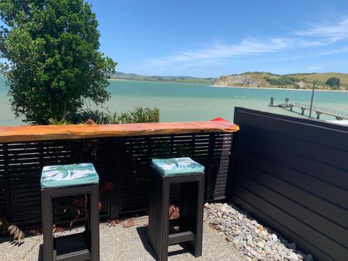 a table and two stools with a view of the water at Beach Lane Apartment in Whangarei