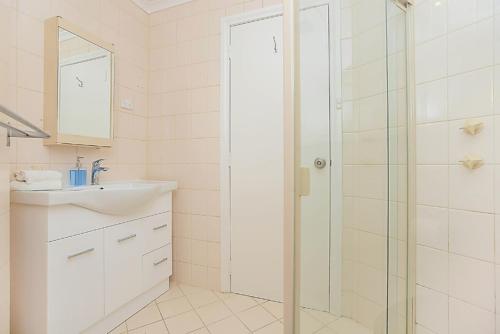 Hi 5 Luxury Holiday Apartments في فيكتور هاربور: حمام أبيض مع دش ومغسلة
