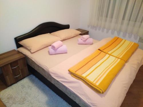 FEEL LIKE HOME في Vrnjačka Banja: سرير عليه نعال وردية اللون ومنشفتين