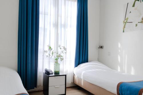 a bedroom with two beds and a window with blue curtains at Hotel Doria in Amsterdam