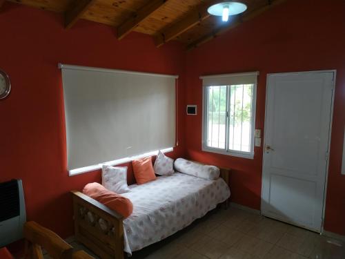 1 dormitorio con 1 cama con paredes de color naranja y ventana en Cabañas Cuncumen en Los Reartes