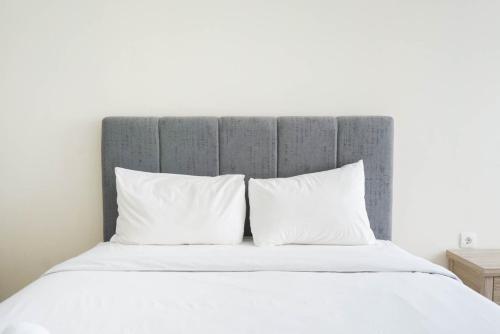 a bed with white pillows and a gray headboard at Minimalist and Homey Studio Menteng Park Apartment By Travelio in Jakarta
