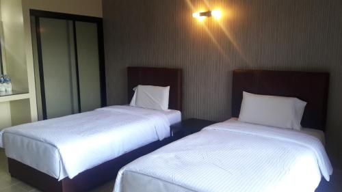 two beds in a hotel room with white sheets at Mana Residence in Hat Yai