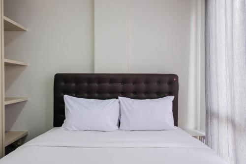 a bed with a black headboard and white pillows at Convenient and Luxurious 2BR Asatti Apartment By Travelio in Pagedangan