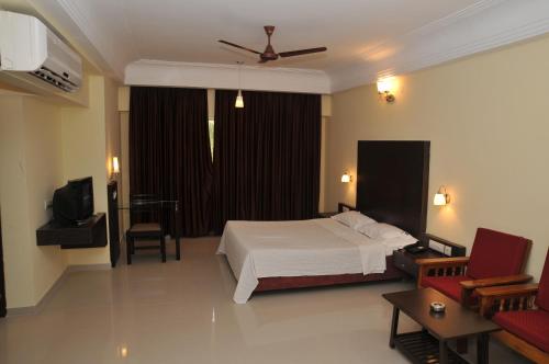 Hotel Vijayentra في بونديتْشيري: غرفة نوم بسرير واريكة وتلفزيون