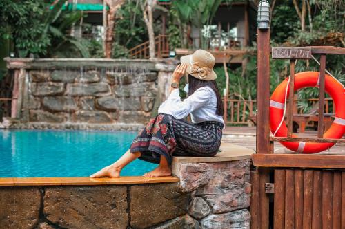 a woman sitting on a surfboard next to a swimming pool at The Vatika Resort and Spa in Ao Nang Beach