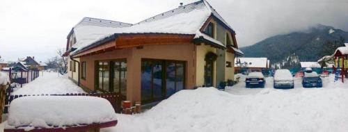 a house covered in snow with cars parked next to it at RELAX PENZIÓN J&L in Pavčina Lehota