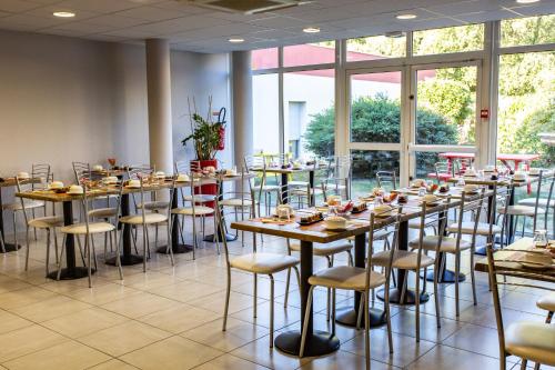 a row of tables and chairs in a room with windows at Hotel The Originals Tours Sud Pic Epeiche (ex Inter-Hotel) in Montbazon