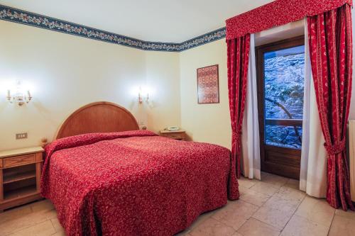 a bedroom with a bed with a red blanket and a window at Hotel Courmayeur in Courmayeur