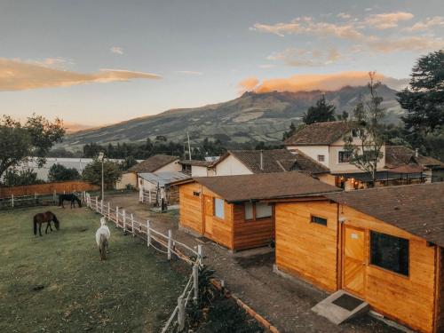 a group of wooden buildings with a horse in a field at Hosteria Papagayo Cotopaxi in Machachi