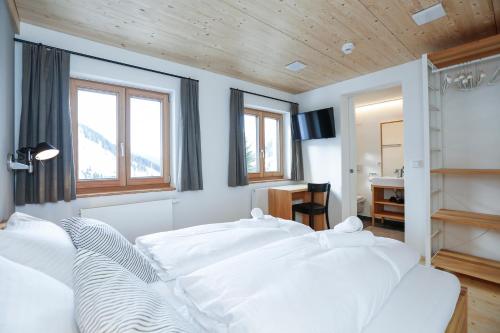 1 dormitorio con cama con sábanas blancas y escritorio en Haus Sonnblick b&b en Stuben am Arlberg
