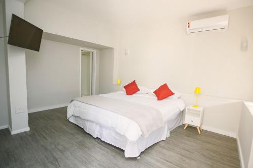 a white bedroom with a large white bed with red pillows at CLH Suites Domingos Ferreira in Rio de Janeiro