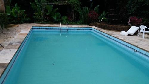 a blue swimming pool with two white chairs in a yard at Rancho Manacá in Guaramiranga