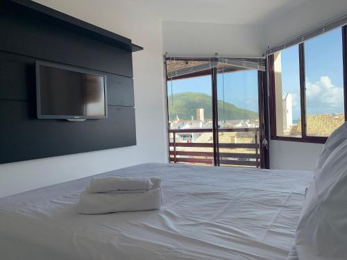 una camera da letto con un letto bianco con una TV a schermo piatto di Apartamento com Vista do Mar em Residencial com Piscina a Florianópolis