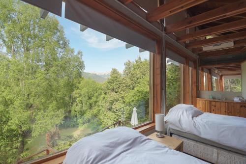 two beds in a room with a large window at Bog Antilhue - Casa 2 cuartos in Villa La Angostura