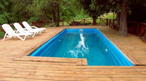una piscina con 2 sillas blancas junto a una terraza de madera en Bog Antilhue - Casa 2 cuartos en Villa La Angostura