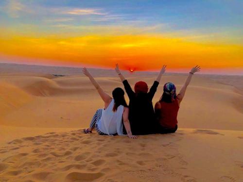 three people sitting on the sand in the desert at Wahiba Bedouin Rustic Camp in Muntarib