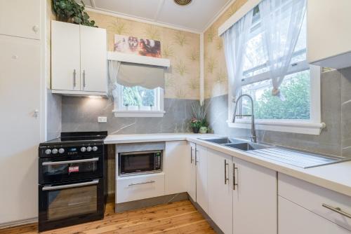 uma cozinha com armários brancos, um lavatório e uma janela em 1 Private Queen room in Carramar 1 Minute Walk To Station em Sydney