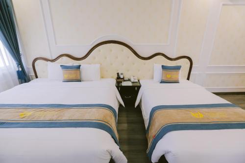 a hotel room with two beds with white sheets and blue pillows at Vincent Halong Hotel in Ha Long