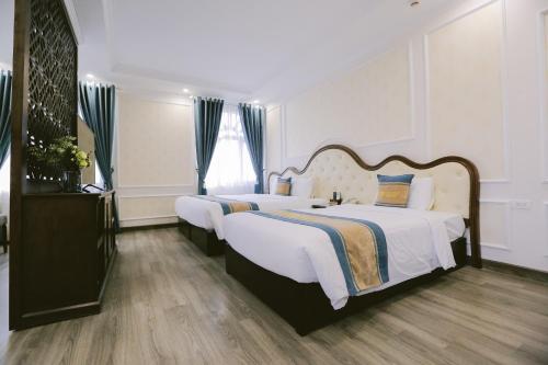 a bedroom with two beds with white sheets and blue curtains at Vincent Halong Hotel in Ha Long