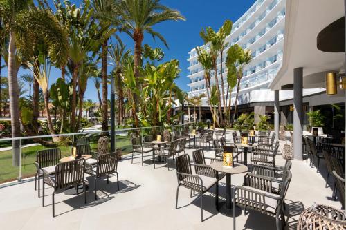 Un patio al aire libre con mesas y sillas y palmeras. en Hotel Riu Palace Palmeras - All Inclusive, en Playa del Inglés