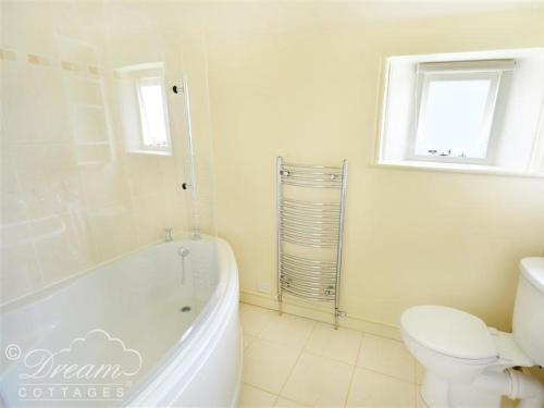 een witte badkamer met een bad, een toilet en een raam bij Coombe Orchard in Swanage