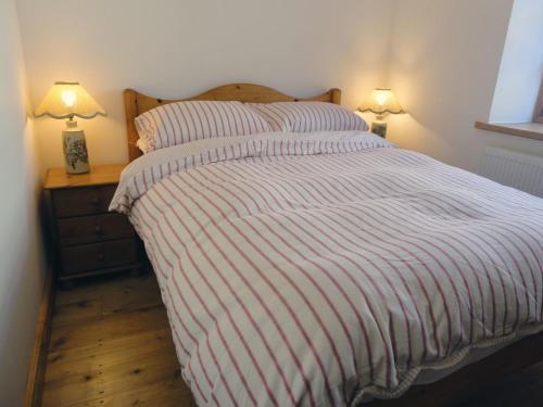 a bed with a red and white striped comforter and two lamps at Mill House Barn in Okehampton