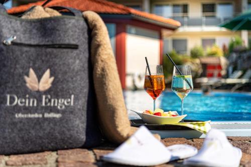 a bag and two glasses of wine on a table next to a pool at Dein Engel in Oberstaufen