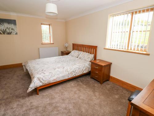a bedroom with a bed and a dresser and two windows at Pant y Gaseg Farm in Ammanford