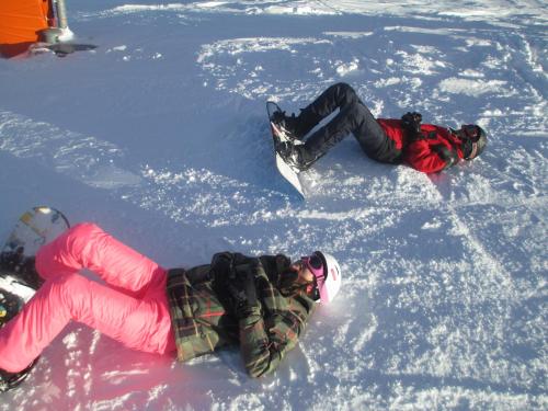 two people laying in the snow with their snowboards at Appt 10p Wifi Confort 150m activités, pistes, commerces in Superdevoluy