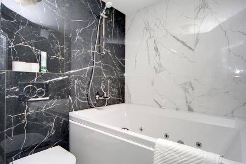a bathroom with a white tub and black marble walls at Arena Summit Apart Hotel in Kyiv