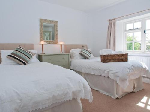 a white bedroom with two beds and a window at Homefield House in Thurlestone