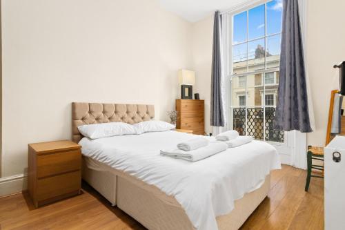 a bedroom with a large bed with white sheets and a window at Spacious 3 Bed Flat with Balcony in Kensington for 6 people in London