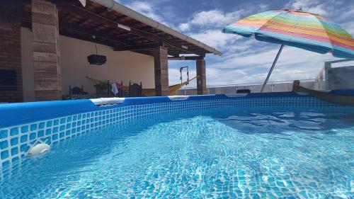 a swimming pool with an umbrella and a person standing in it at Mirante Beach House in Piaçabuçu