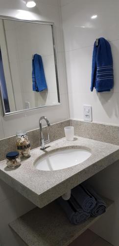 La salle de bains est pourvue d'un lavabo, d'un miroir et de serviettes bleues. dans l'établissement Apto 1110 - Golden Village Taperapuã, à Porto Seguro
