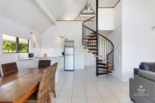 a kitchen and dining room with a wooden table and a spiral staircase at Cardwell Beachcomber Motel & Tourist Park in Cardwell