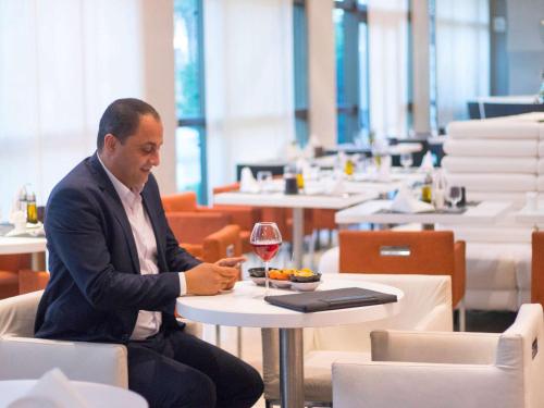 a man sitting at a table with a glass of wine at Novotel Tunis in Tunis