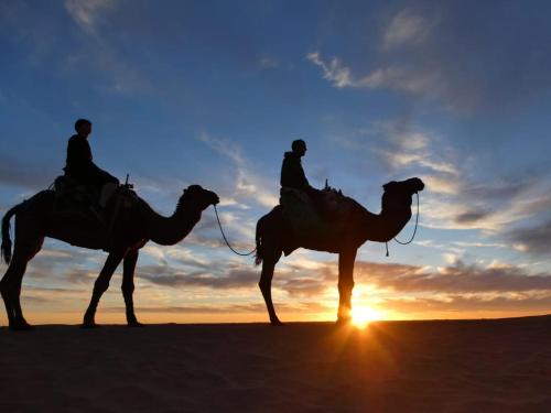 two people riding camels in the desert at sunset at Desert Atmosphere M'Hamid in Mhamid