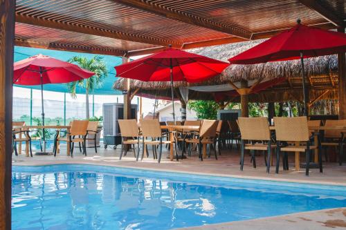 a pool with tables and chairs and red umbrellas at Hotel Maioris Navolato in San Pedro