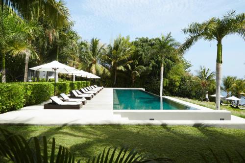 una piscina con tumbonas, sombrilla y palmeras en Boutique Hotel The Lombok Lodge, en Tanjung