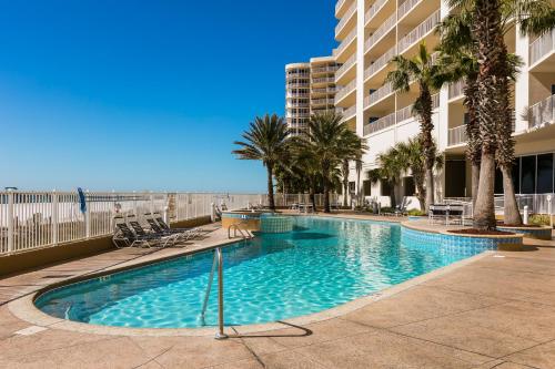 a swimming pool with palm trees and a building at Admirals Quarters in Orange Beach