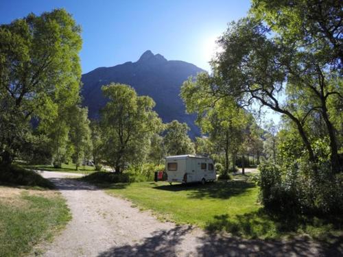 a white truck parked in a grassy area next to a forest at Trollveggen Camping in Åndalsnes