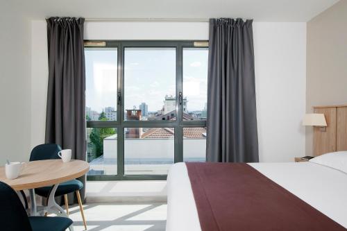 Cette chambre comprend un lit, une table et une grande fenêtre. dans l'établissement Residhome Lyon Gerland, à Lyon