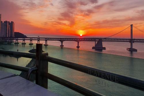 eine Brücke über das Wasser mit dem Sonnenuntergang im Hintergrund in der Unterkunft H Avenue Hotel Gwangalli branch in Busan